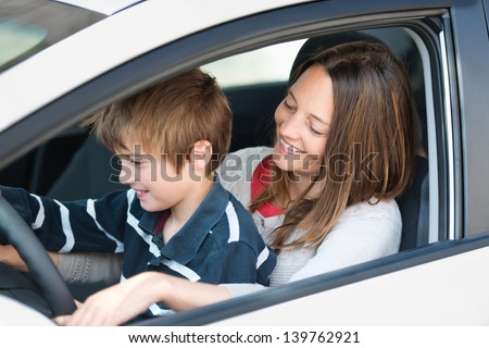 Smiling mother teaching her son how to drive a car