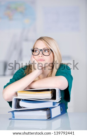 Young overworked businesswoman with stack of binders at office desk