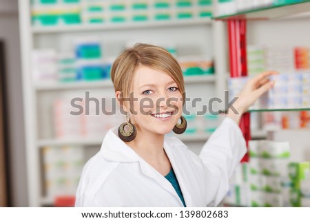 Portrait of young female pharmacist choosing medicine from shelf