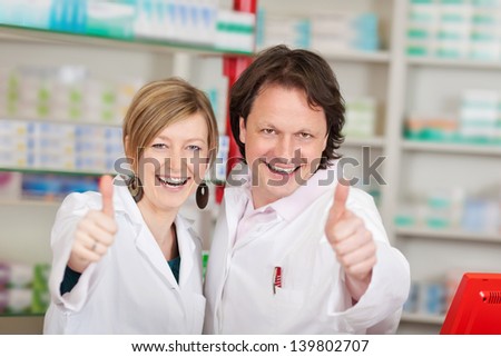 Portrait of happy pharmacists showing thumbsup sign in pharmacy