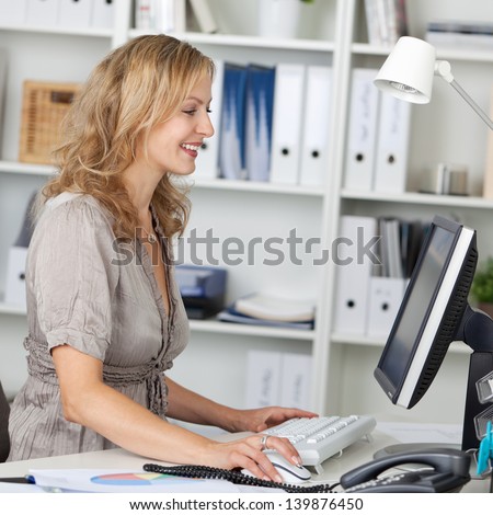 Side view of happy businesswoman using computer at desk in office