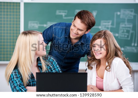 Portrait of young confident male and female students with laptop at desk