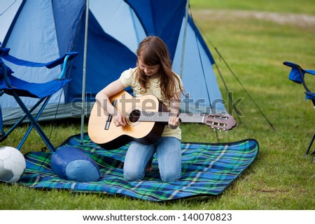 Young girl playing guitar against blue tent at field
