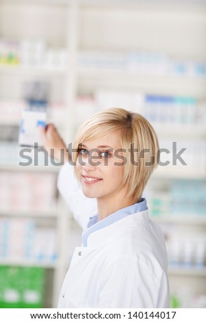 Portrait of young female pharmacist taking out medicine from shelf in pharmacy