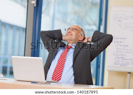 Relaxed mature businessman with hands behind head at office desk