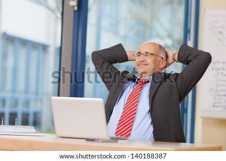 Relaxed businessman with hands behind head sitting at office desk