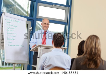 Happy businessman giving presentation to coworkers while standing at podium in office