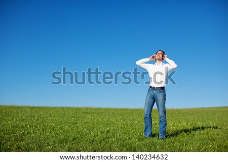 Blissful man enjoying his music outdoors standing in a fresh green field under a sunny blue sky with his head tilted back in pleasure, with copyspace