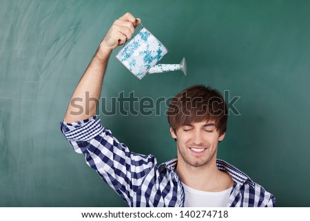 Portrait of handsome young male student holding watering can representing growth of ideas