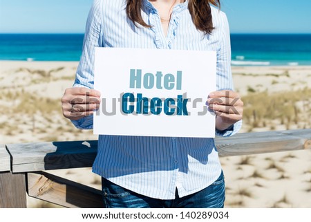 Midsection of woman holding Hotel Check sign at beach