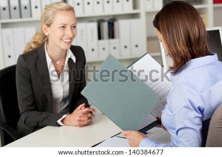 Mid adult businesswoman reading female candidate\'s CV at office desk