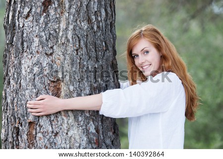 Pretty woman hugging a tree standing with her arms around the trunk smiling at the camera to show her appreciation