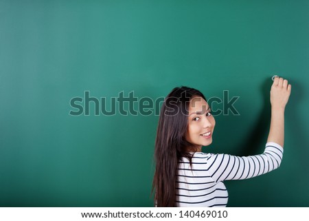 smiling student writing on empty blackboard looking back over shoulder