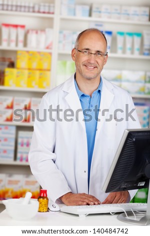 Portrait of confident mature pharmacist standing at counter in pharmacy