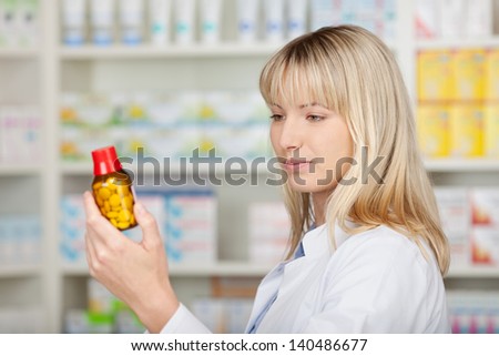 Young female pharmacist looking at medicine bottle in pharmacy