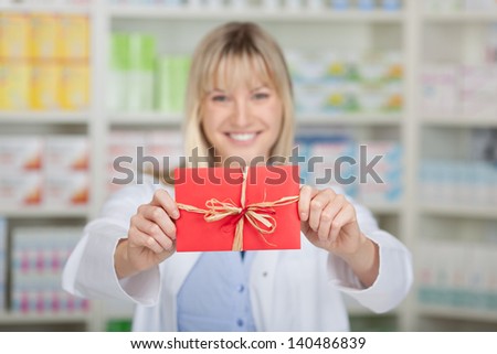 Portrait of happy female pharmacist holding wrapped gift in pharmacy