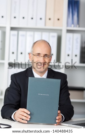mature businessman holding application book at office table