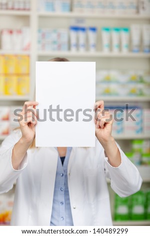 Female pharmacist holding blank paper in front of face in pharmacy