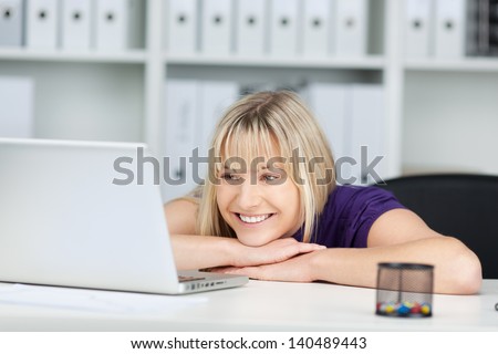 Young businesswoman looking at laptop while leaning at office desk