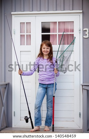 Portrait of cute girl holding fishing net and rod at camping house