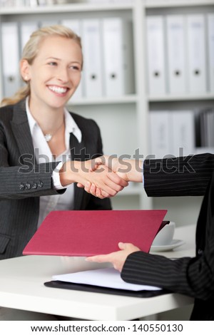 Happy young businesswoman shaking hands with candidate during an interview at desk
