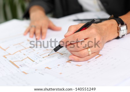 Closeup of female architect\'s hands working on blue print at desk