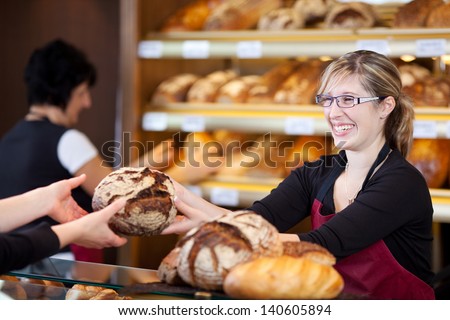 friendly saleswoman in bakery passing bread over the counter
