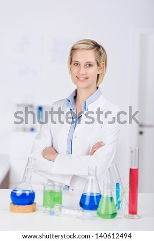 Portrait of confident female scientist with arms crossed standing at desk