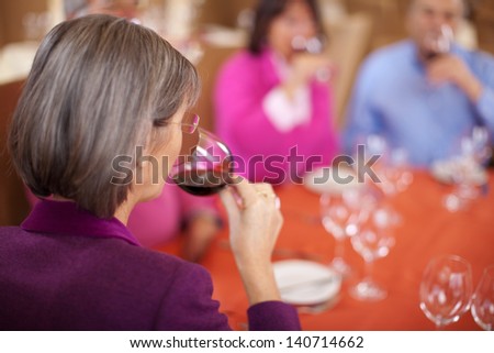 elderly woman drinking wine with friends in restaurant