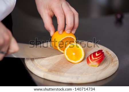 Closeup of chef's hand cutting orange for garnishing in commercial kitchen
