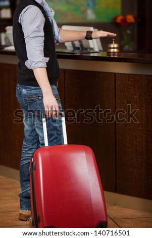 Low section of male customer with baggage ringing bell at reception counter of hotel