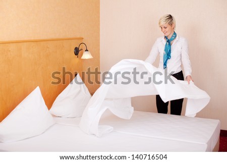 Young female housekeeper making bed in hotel room