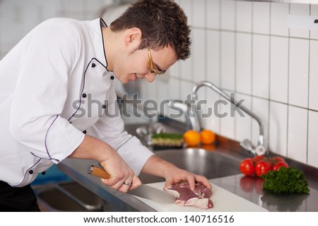 Young chef cutting meat on chopping board at commercial kitchen
