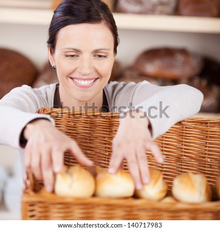 Smiling happy woman worker with a friendly smile sorting fresh rolls in a bakery in a large wicker basket