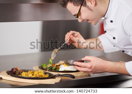 Closeup of chef garnishing egg dish with sauce in commercial kitchen