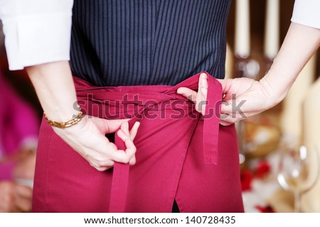Rear midsection of waitress tying apron in restaurant