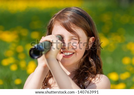 Closeup of happy young girl looking through telescope in park