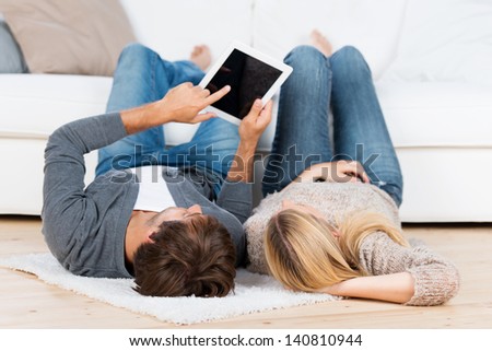 man lying on the floor showing something on tablet to his girlfriend