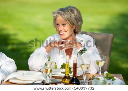 Happy senior woman with hands clasped looking away at dining table in lawn