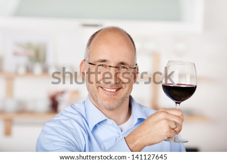 Smiling man showing the red wine at home