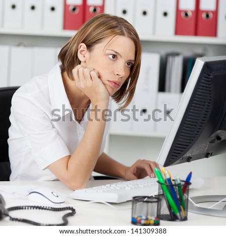 Office worker reading her computer monitor concentrating on the information while seated at her desk