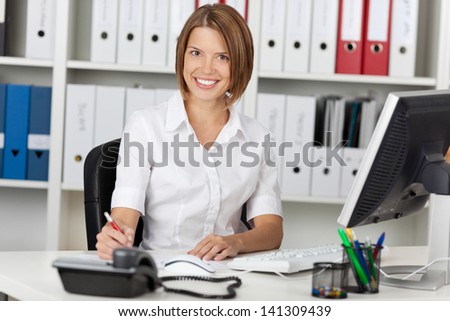 Smiling confident businesswoman sitting at her desk in the office in front of a desktop computer