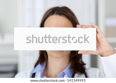 Closeup of female doctor holding blank paper in front of her face