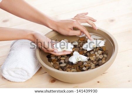 Female hands placing white orchids onto a bowl with pebbles filled with water so that they float on the surface in a spa treatment concept