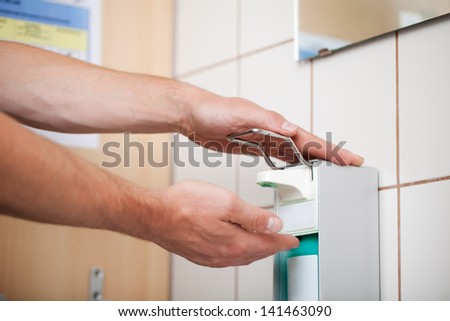 Closeup of male doctor\'s hands using sanitizer dispenser in washroom
