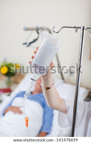 Nurse adjusting infusion bottle with patient in bed in hospital