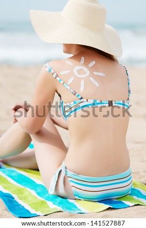Rear view of a young woman in bikini and sunhat with sun drawn on back at beach