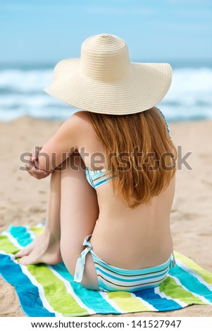 Rear view of a young redhead woman in bikini and sunhat enjoying the sea view at beach