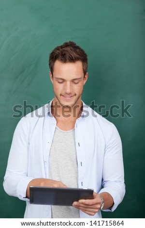 Serious young male executive using digital tablet against green background