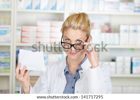Portrait of a female pharmacist with prescription looking over glasses at drugstore